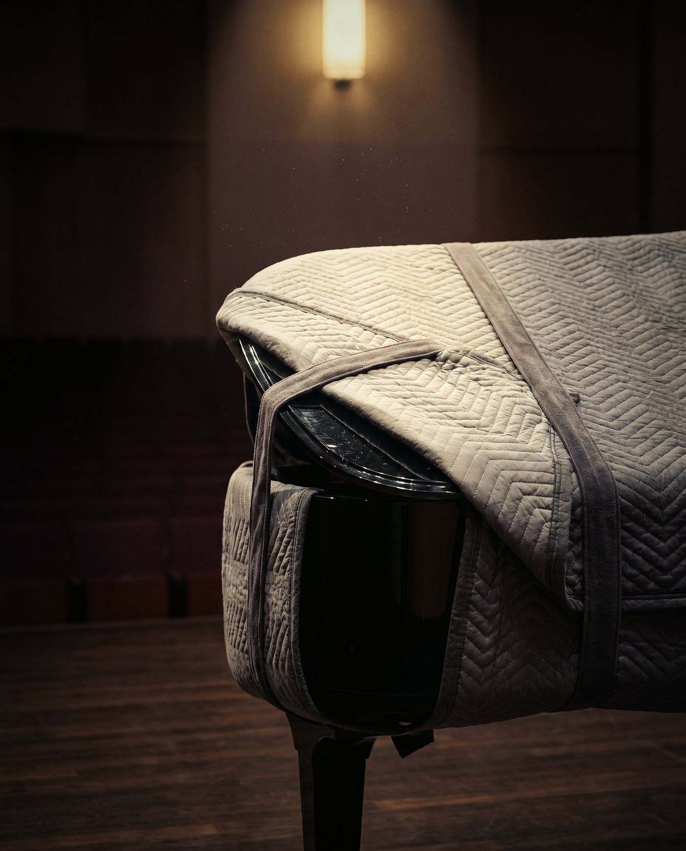 A black grand piano in a padded grey cover, held with soft straps